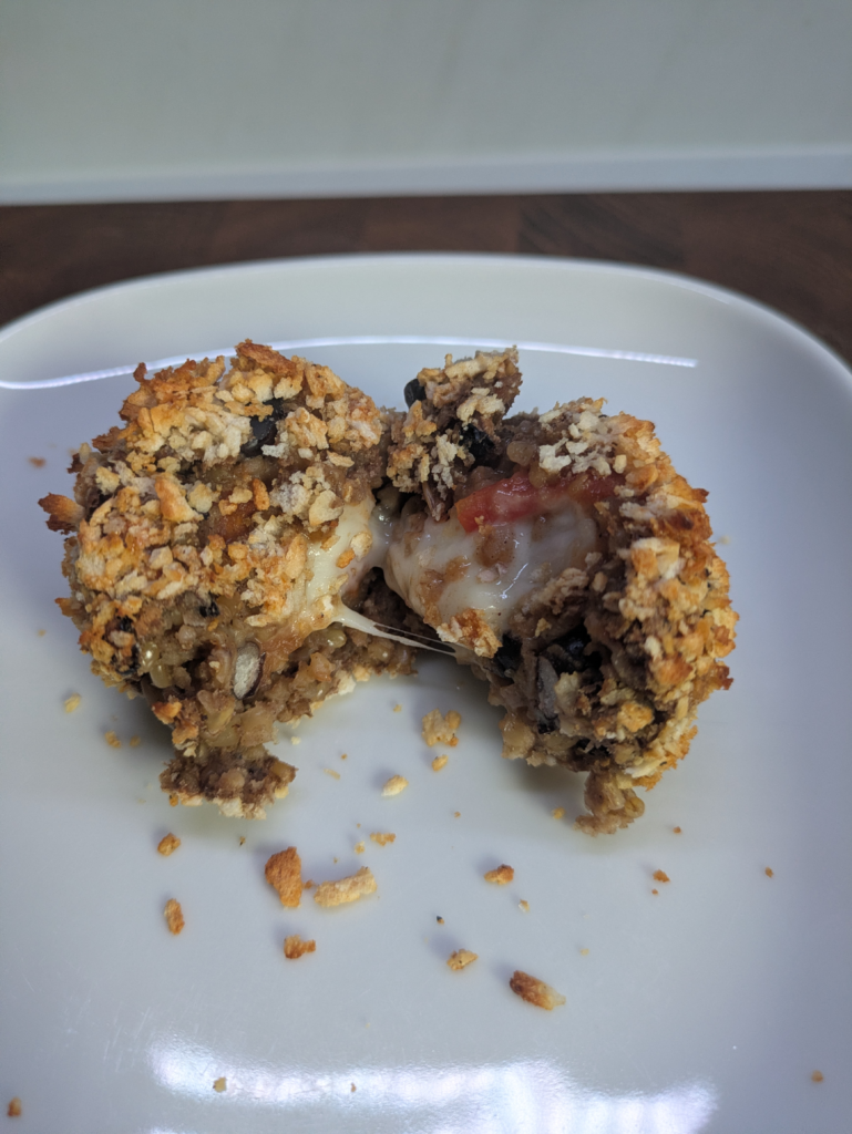 A haggicini ball that has been cut in half and pulled away to show the melted mozzarella inside of the haggis ball together with the tomato chutney. The image is to show the inside.