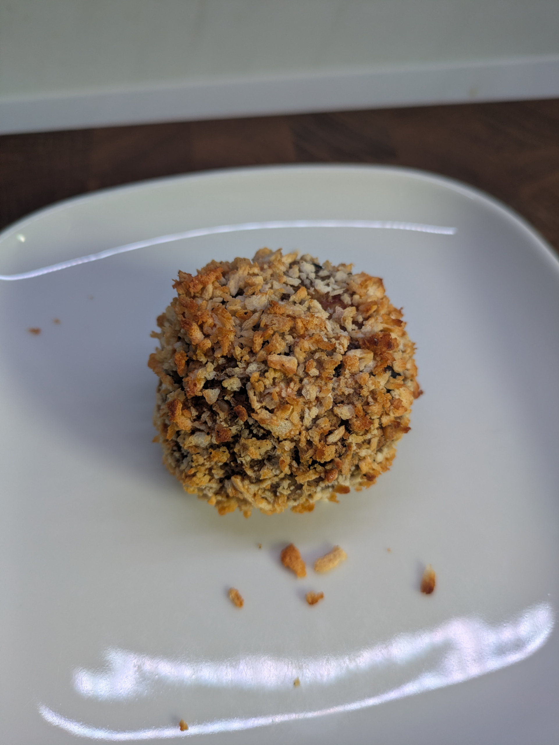 A ball covered in golden panko breadrumbs on a white plate. It has not been cut so it is whole.